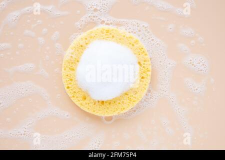 Éponge cosmétique beige naturel avec mousse nettoyante sur fond pastel. Routine de beauté le matin ou le soir. Concept de soins de beauté pour le visage. Vue de dessus Banque D'Images