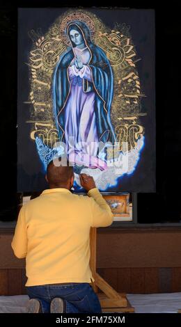 Un artiste ajoute une touche finale à une peinture de la Vierge Marie ou de notre Dame de Guadalupe devant une galerie d'art à Santa Fe, Nouveau-Mexique. Banque D'Images