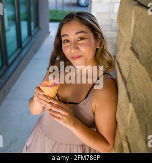 Petite Jeune femme asiatique Eating réaliste Rainbow Sherbet glace Dans un cône de gaufrage en milieu urbain Banque D'Images