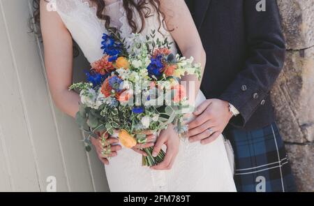 Gros plan des mains de mariée et de marié tenant des fleurs Banque D'Images