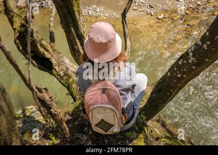 Prise de vue en grand angle d'UNE fille assise dans la canopée au-dessus de la rivière et profitant de la belle Journée du soleil dans la nature. Banque D'Images