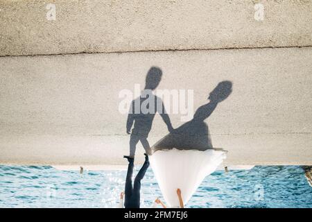 Silhouettes sur l'asphalte de la mariée et marié qui marchez le long de la route par la mer en tenant les mains Banque D'Images