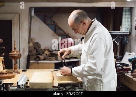 Ébéniste dans son atelier marquant un morceau de bois avec une boussole de mise en plan Banque D'Images