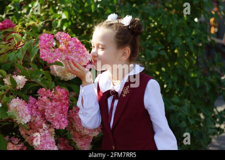 Adorable petite fille d'école portant uniforme fille danse et sourire dehors dans le jardin de fleurs lors d'une belle journée ensoleillée. Banque D'Images