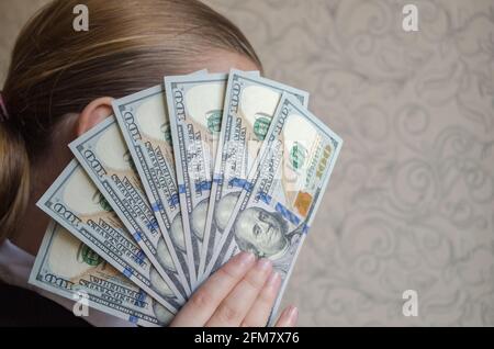 Un wad de billets de cent dollars, ouvert sous la forme d'un ventilateur, couvre le visage d'une jeune fille caucasienne avec des cheveux bruns tirés dans un stang de queue de cheval Banque D'Images