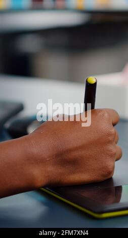 Gros plan sur l'éditeur de photo africain dessin sur tablette graphique retouche photo client sur ordinateur avec deux moniteurs. Retouche noire tenant un stylet pour retoucher des documents dans un bureau d'agence de création Banque D'Images