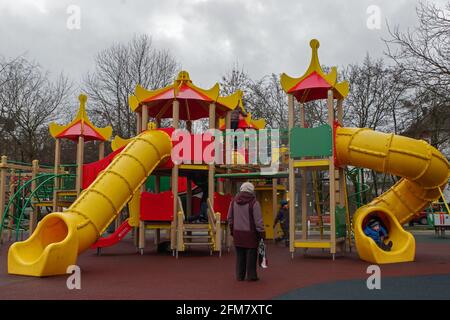 Le terrain de jeu est un complexe de tours avec des toits rouges reliés par plates-formes avec tuyaux jaunes-toboggans avec des enfants s'amuser dessus et grand-mère en attente Banque D'Images