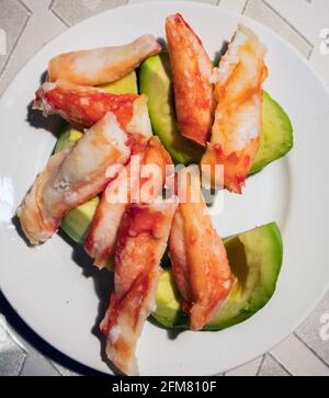 Pattes de crabe pelées et cuites sur une assiette blanche avec des tranches d'avocat mûr Banque D'Images