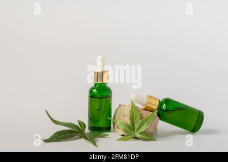 Flacons en verre vert avec huile de CBD, teinture de THC et feuilles de chanvre sur fond blanc. Style minimaliste. Cosmétiques biologiques cosmétiques à l'huile CBD Banque D'Images