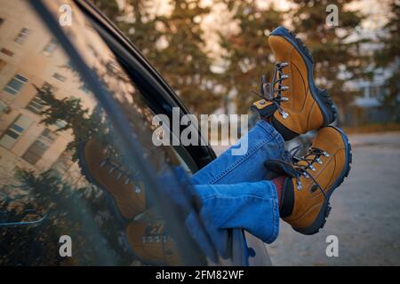 Femme pieds dans des bottes de randonnée jaune tendance sur la porte de voiture. Pieds à l'extérieur de la fenêtre au coucher du soleil forêt. Le concept de liberté de mouvement. Un week-end d'automne Banque D'Images