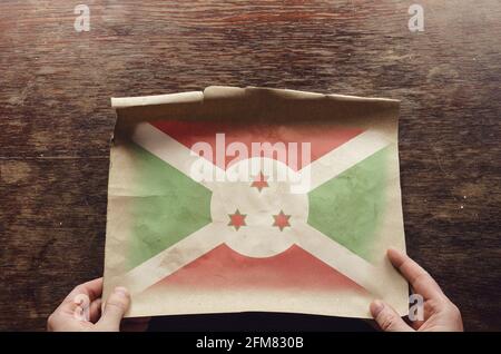 Le drapeau national du Burundi sur un morceau de papier déchiré. Les mains d'un homme pressaient une feuille de parchemin dépliée sur une table en bois marron. Vue de dessus Banque D'Images