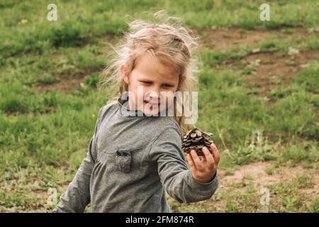 L'enfant tient un cône de pin dans ses mains. Portrait des enfants. Blonde fille de 4 ans. L'homme et la nature. Le bébé joue dans la nature. Banque D'Images