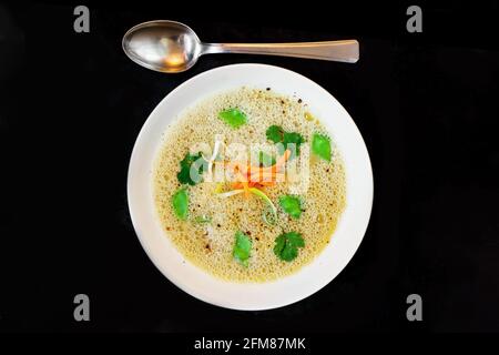 Soupe fouettée à la purée d'asperges avec julienne d'herbes et de légumes dans une assiette blanche sur fond noir. Banque D'Images