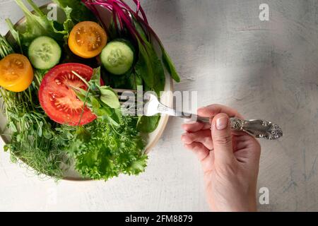 Mélanger les salades, le concombre, les tomates rouges et jaunes dans l'assiette et à la main avec la fourchette. Jeunes pousses juteuses de pois ou de haricots, pousses de betteraves, salade verte et légumes Banque D'Images