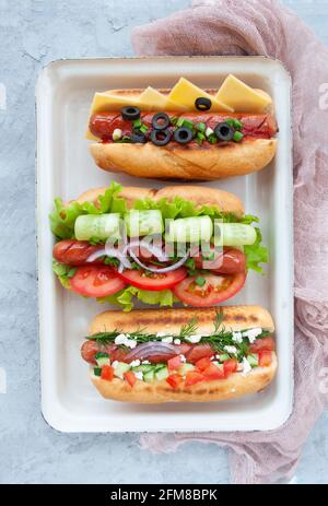 Délicieux hot dogs fraîchement cuits avec saucisses, légumes, fromage et sauce vue de dessus. Banque D'Images