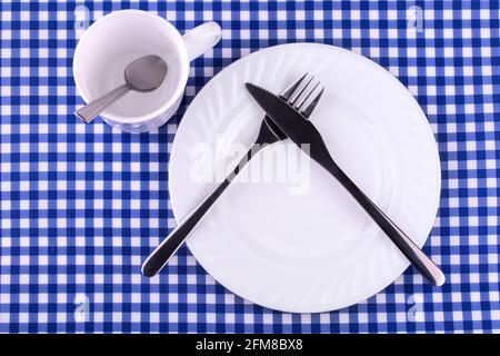 Empy Mug avec cuillère, assiette avec un couteau et fourchette sur la nappe dans une cage. Vue de dessus avec espace de copie Banque D'Images