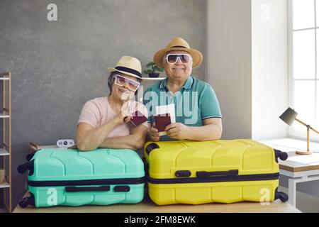 Portrait d'un couple senior mignon et heureux avec billets d'avion, passeports et valises à la maison Banque D'Images