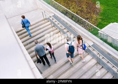 Un groupe de personnes descend les escaliers. Escalier en béton avec rampes, rampe et herbe verte. Intérieur urbain. Vue de dessus. Banque D'Images