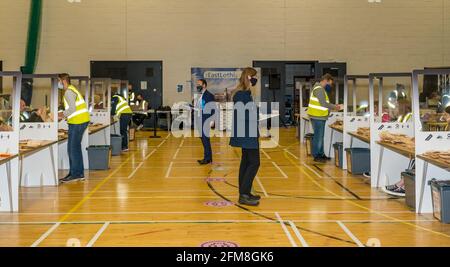 Meadowmill Sports Center, East Lothian, Écosse, Royaume-Uni. 7 mai 2021. Les élections parlementaires écossaises comptent pour la circonscription de Lothian est : le personnel du directeur du scrutin trie les bulletins de vote et compte les votes tandis que les agents candidats regardent porter des masques faciaux et socialement distancés Banque D'Images