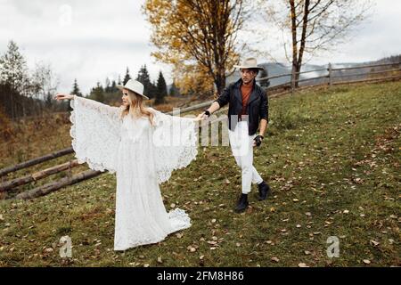 Charmant homme beau tenir une main de magnifique belle femme en robe de mariée blanche, marchant sur le terrain, appréciant des moments ensemble. Adorable Banque D'Images