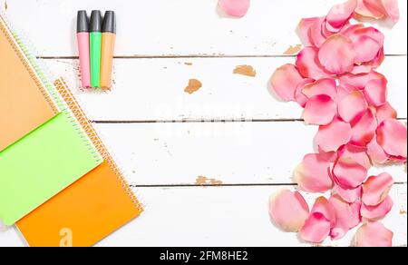 Photo de lampes fluorescentes colorées et de divers carnets sur un arrière-plan en bois blanc et orné de pétales de rose.la photo est un cliché en tête avec Banque D'Images