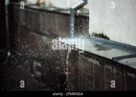 les gouttes de pluie tombent cassent sur la corniche. projections d'eau courante. drainpipe du toit d'un bâtiment pendant une tempête Banque D'Images