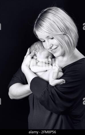 Photo en niveaux de gris d'une mère caucasienne qui embrasse son nouveau-né isolé sur fond noir Banque D'Images