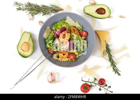 Vue de dessus d'un bol bleu moderne avec pâtes, fruits de mer, avocat, tomates et feuilles fraîches vertes sur fond blanc. Concept de belle composition avec des légumes et du fromage savoureux et des herbes. Banque D'Images