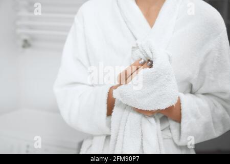 Vue de face de la jeune femme en robe debout dans la salle de bains avec une serviette blanche après la douche et les mains essuyeuses. Concept de procédure spéciale d'eau pour le corps de soin à la maison. Banque D'Images