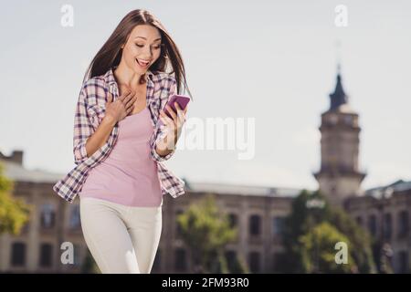 Photo de la jeune fille heureux sourire positif stupéfié surprise choquée regardez lire sms téléphone portable université campus en plein air Banque D'Images