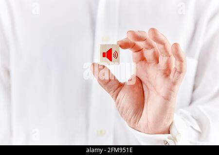 La main mâle contient un cube en bois avec une icône de haut-parleur. Concept d'augmentation du volume sonore. Banque D'Images