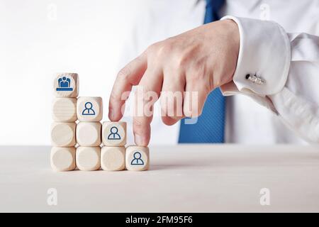 Main d'un homme d'affaires grimpant sur l'échelle de carrière en cubes de bois avec des icônes d'employés. Concept d'amélioration de carrière, de promotion et de planification. Banque D'Images