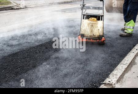 l'ouvrier rampe l'asphalte sur la route avec un rameur mécanique. pose de la surface de la route. asphalte chaud sous la pression du rameur Banque D'Images