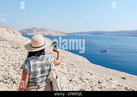 Vue arrière de la femme prenant des photos avec vue spectaculaire sur la mer et le littoral en été. Banque D'Images