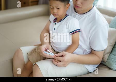 Le père asiatique utilise des tondeuses pour couper les ongles de son fils dans le salon, les pères interagissent avec leurs enfants tout au long de la journée. Banque D'Images