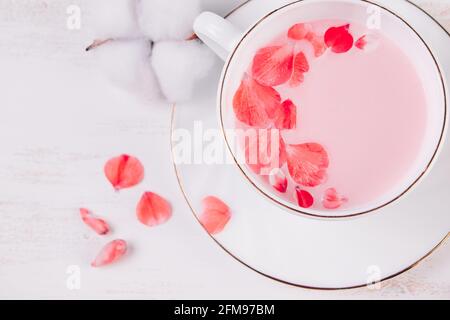 Thé végétalien tendance sur fond blanc. Matcha rose avec pétales de rose dans une tasse. Recette de boisson relaxante pour les moments de sommeil. Banque D'Images