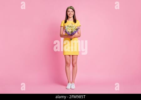 Vue sur toute la longueur de la taille du corps d'une jolie fille gaie tenue dans les mains fleurs sauvages isolées sur fond de couleur rose Banque D'Images