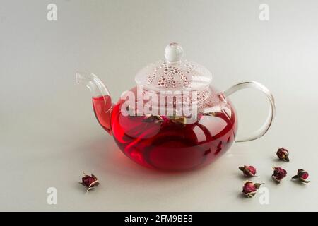 Thé rose avec roses dans la théière en verre sur fond gris. Gros plan. Copier l'espace. Banque D'Images