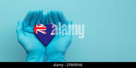 Médecins mains portant des gants chirurgicaux tenant le cœur du drapeau australien Banque D'Images