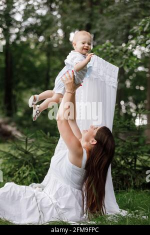 Bonne femme belle, jeune mère jouant et se lancer avec son adorable bébé fils, mignon petit garçon, en appréciant ensemble une journée ensoleillée chaud jouant dessus Banque D'Images