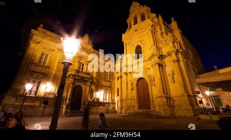 Italie, Sicile, Sicile du Sud-est, angle baroque, Ragusa, Ragusa la nuit, église illuminée Chiesa di San Giuseppe, vue grand angle extrême de la diagonale en dessous, au premier plan à gauche est une lumière de rue lumineuse et étincelante, peu de personnes floues Banque D'Images