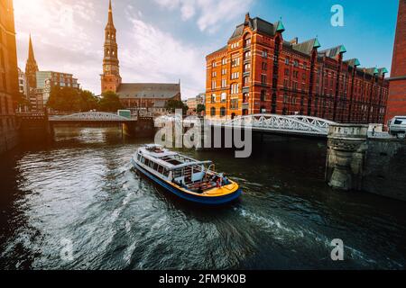 Bateau de croisière touristique sur un canal avec des ponts dans l'ancien quartier d'entrepôts Speicherstadt à Hambourg en heure d'or coucher de la lumière, de l'Allemagne. Banque D'Images