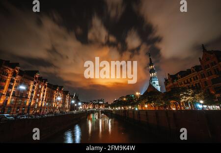 Quartier des entrepôts Speicherstadt de Hambourg la nuit avec vue du pont vers l'église Sainte-Catherine et Elbphilharmonie. Paysage urbain la nuit. Les lumières réfléchissement sur l'eau et le ciel. Banque D'Images