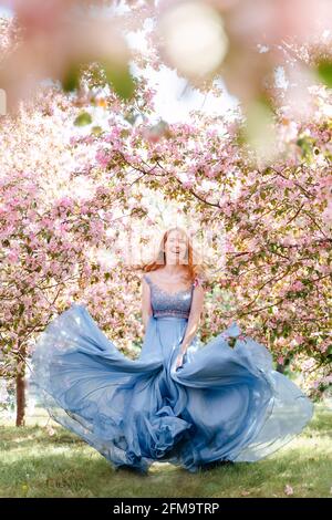 Fille souriante dansant dans une robe sur un fond d'un jardin de roses. Banque D'Images