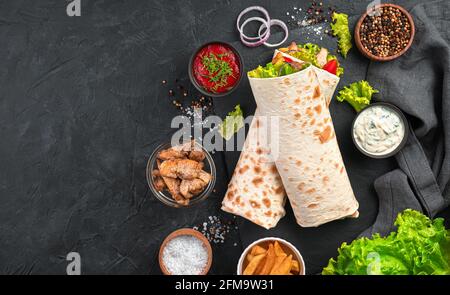 Shawarma avec légumes, salade et poulet sur fond noir avec ingrédients. Vue de dessus, espace de copie. Banque D'Images