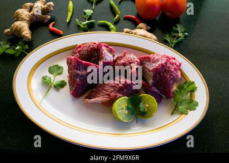 Steaks de bœuf frais décorés de légumes et d'herbes sur une assiette blanche, sélective. Banque D'Images