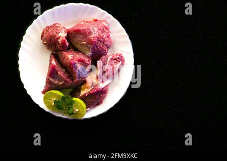 Steaks de bœuf frais décorés de légumes et d'herbes sur une assiette blanche, sélective. Banque D'Images