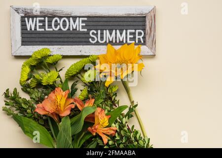 Bouquet avec Alstroemeria, mini-chrysanthèmes verts et petit tournesol jaune sur fond jaune pâle avec panneau de feutre d'été de bienvenue Banque D'Images