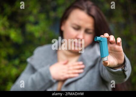 Jolie jeune femme brunette ayant une crise d'asthme. Elle tient un inhalateur. Femme asthmatique utilisant un inhalateur d'asthme pendant les crises d'asthme, soins de santé Banque D'Images