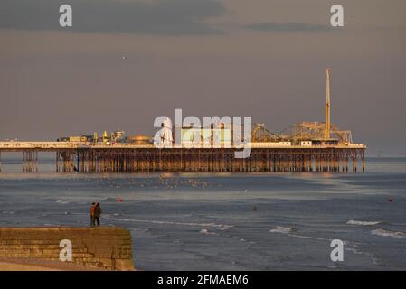 Couple n un groyne avec Brighton's Palace Pier dans l'après-midi lueur d'un coucher de soleil. Brighton & Hove, Sussex, Angleterre, Royaume-Uni Banque D'Images